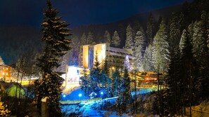 Un bâtiment doté d’une tour imposante, entouré d’arbres couverts de neige et bordé d’un chemin illuminé.