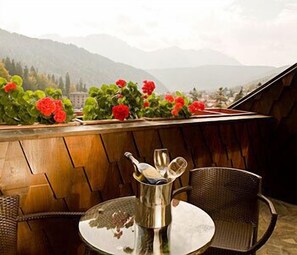 Une table avec un récipient en métal et un verre, placée devant un mur en bois, avec vue sur des montagnes et des fleurs.