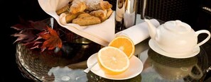 Une table avec un panier de viennoiseries, une théière et un verre de jus d’orange.