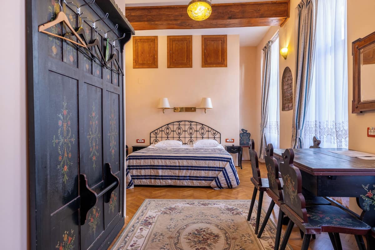 A bedroom with a bed, a desk, and a chair. There is a wardrobe with a mirror and a light fixture above the bed.