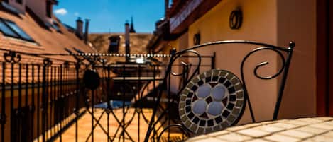 A tiled outdoor area with a metal fence, a mosaic table, and a view of buildings in the background.