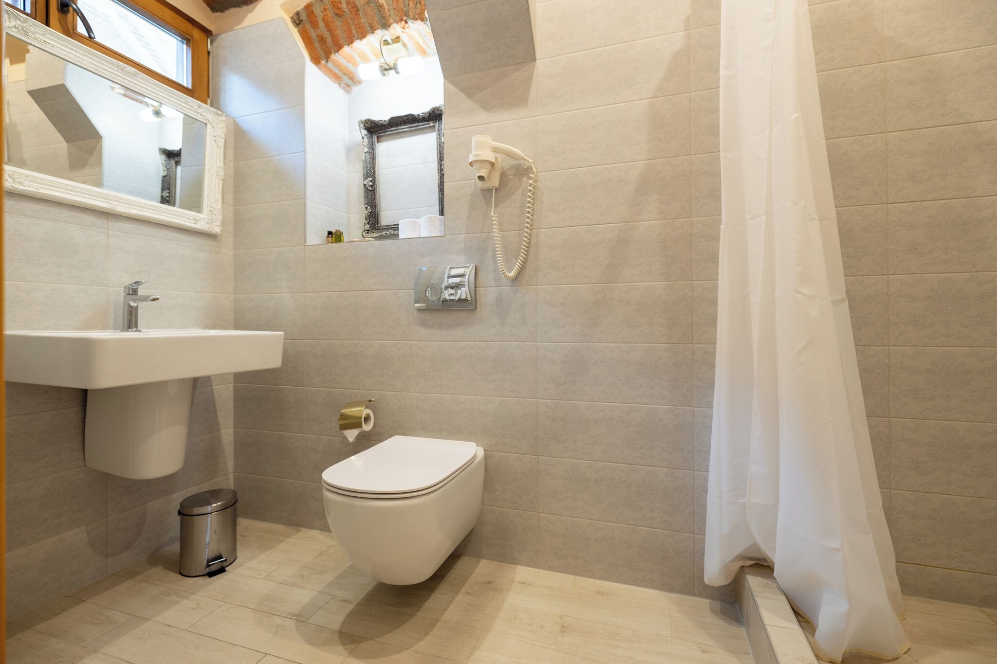Un baño con lavamanos, inodoro y secador de pelo fijado a la pared.
