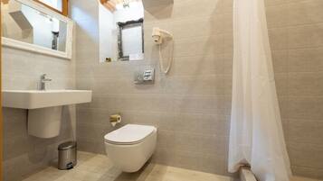 Un baño con lavamanos, inodoro y secador de pelo fijado a la pared.