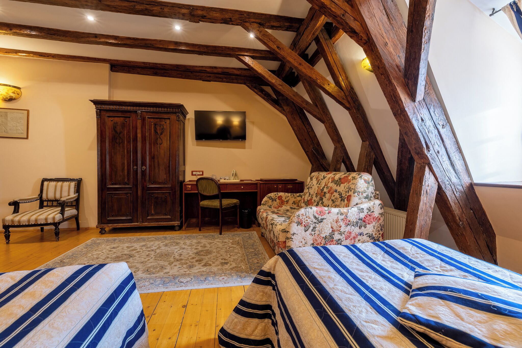 Een slaapkamer met houten balken, een bureau, een stoel, een bank en twee bedden.
