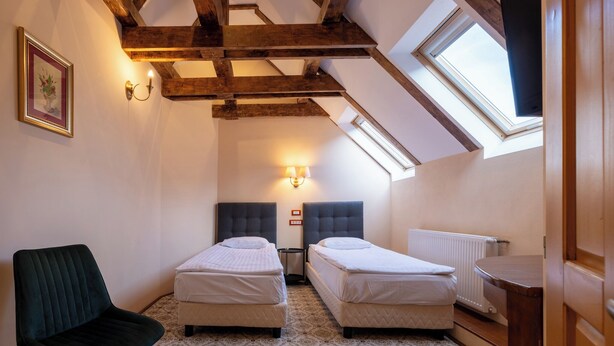 Una habitación pequeña y acogedora con dos camas individuales, una silla, una lámpara de pared y un tragaluz.