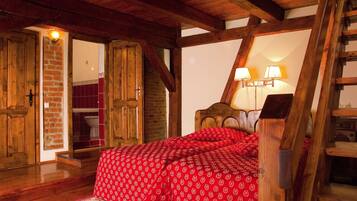 Un dormitorio con techo de madera, una cama con ropa de cama roja, una pared de ladrillo y una escalera de madera.