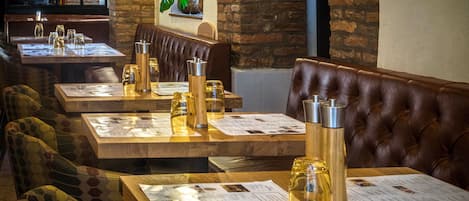 Un interior de restaurante con mesas de madera, asientos tipo banqueta de cuero y tarjetas de menú.