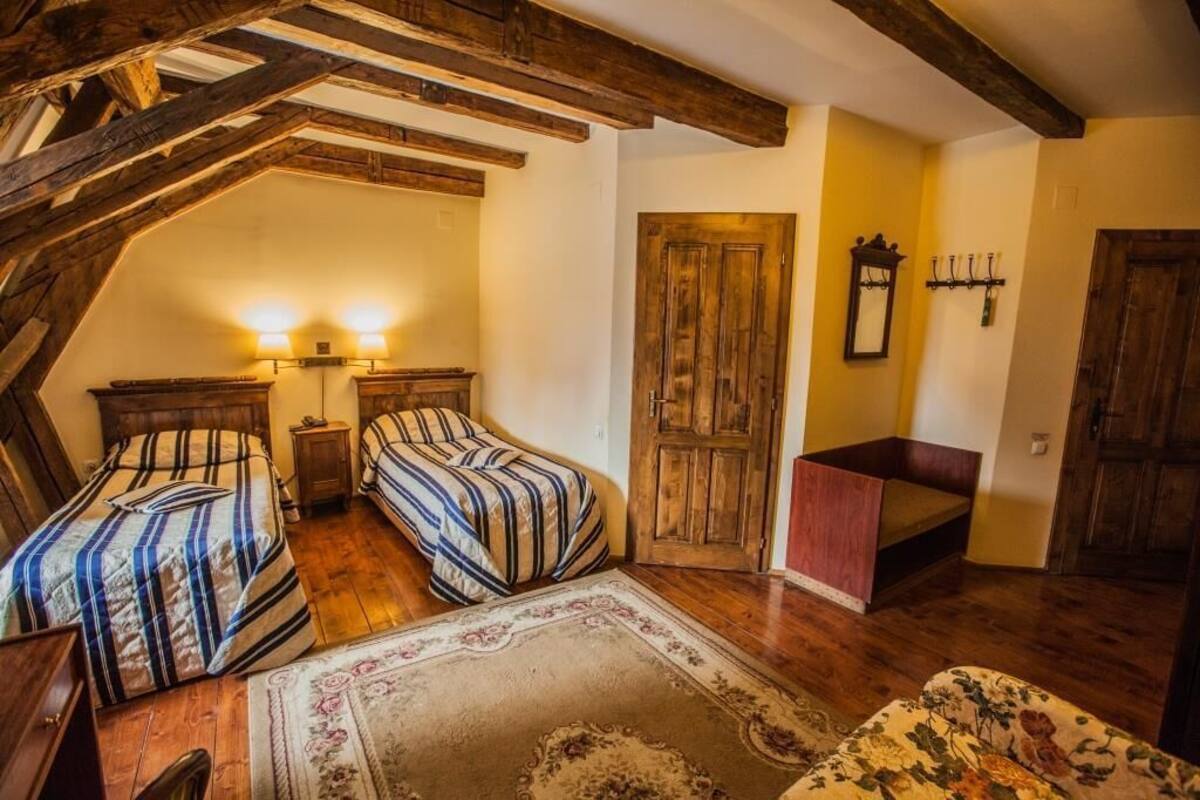 A bedroom with two beds, wooden beams, a wooden door, and a small bench.