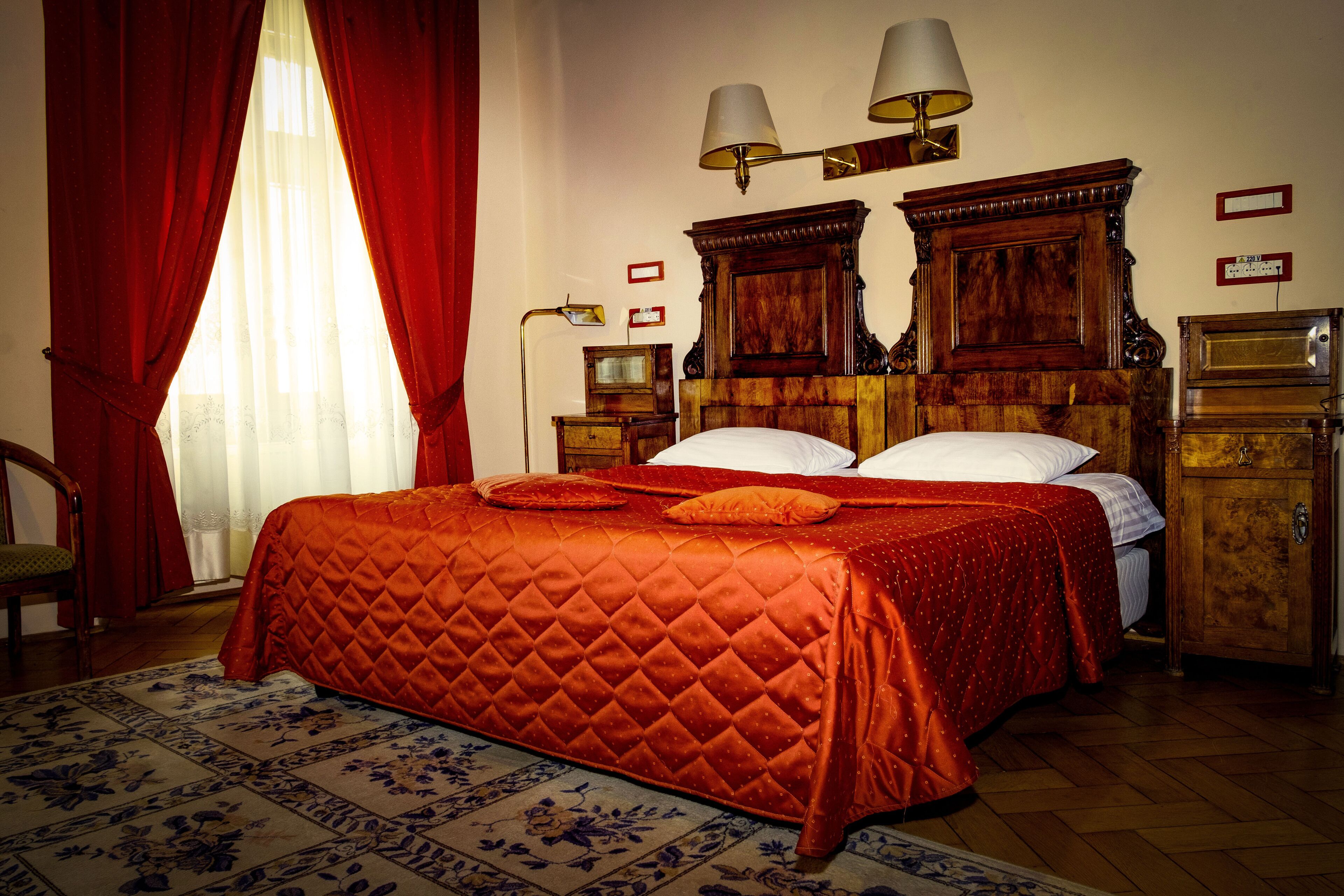 A hotel room with a large bed, two bedside lamps, a wooden headboard, a nightstand, a wooden wardrobe, and a floral-patterned rug.