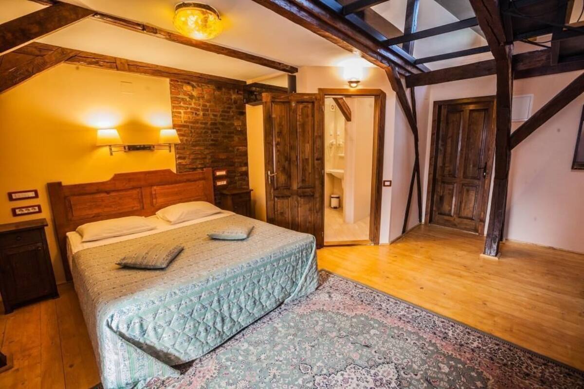 A bedroom with a wooden bed, a nightstand, a wall-mounted light, a door, and a staircase.