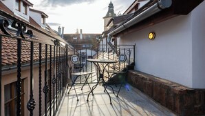 A narrow alleyway with a small outdoor seating area featuring a table and chairs, a metal railing, and a building with a tiled roof and a tower in the background. - Casa Wagner Brasov (Brasov)