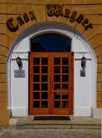La entrada al Hotel Casa Wagner, con una puerta de madera con paneles de vidrio, flanqueada por dos faroles y un arco decorativo.