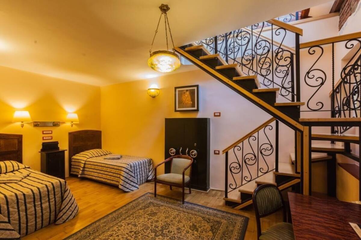 A cozy room with two beds, a chair, a table, and a staircase with decorative railings.