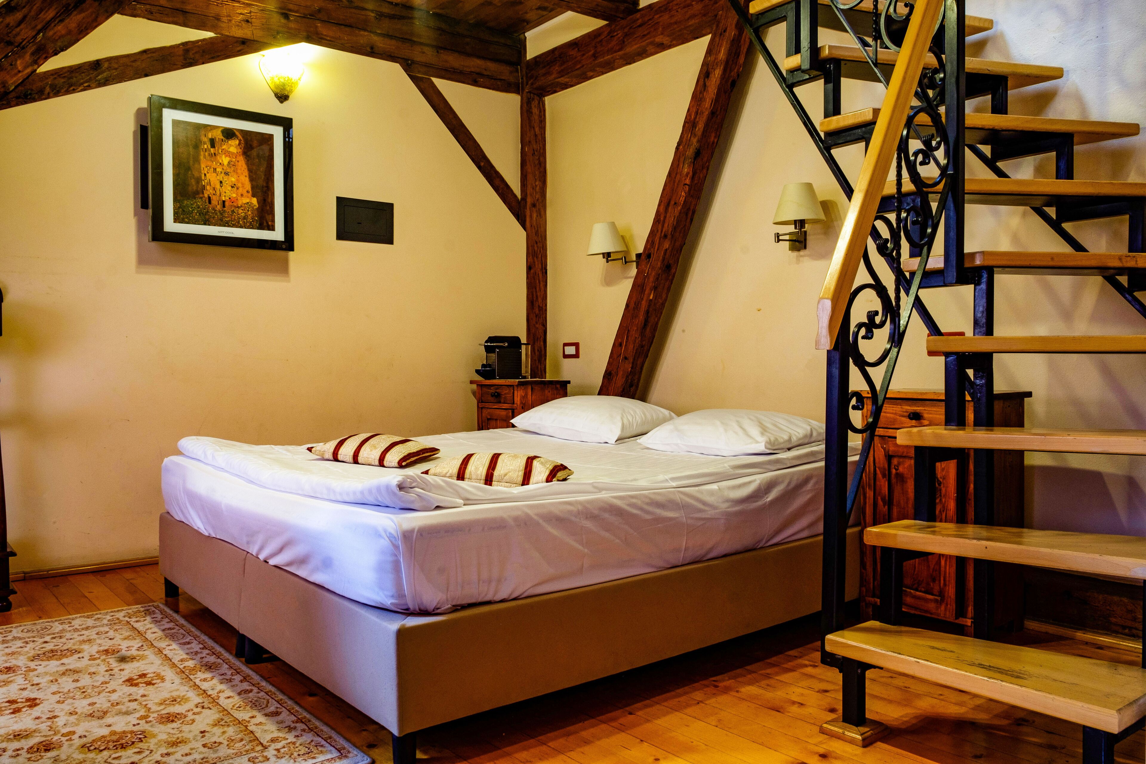 Quarto com cama, piso de madeira, escada e um quadro na parede.