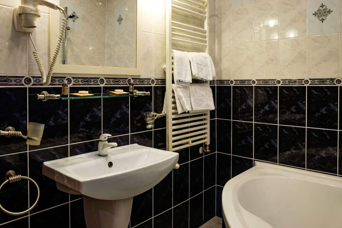A bathroom with a sink, a bathtub, a towel rack, a glass shower enclosure, and a hand dryer.