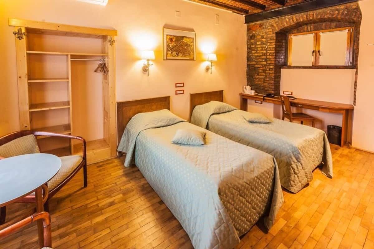 A room with two beds, a wooden desk, a chair, and a wardrobe.