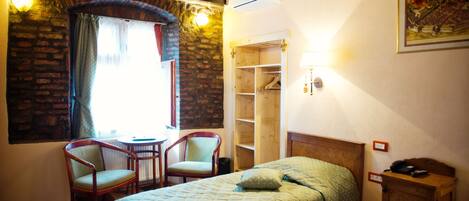 Una habitación con cama, dos sillas, un armario de madera y una ventana con cortinas.