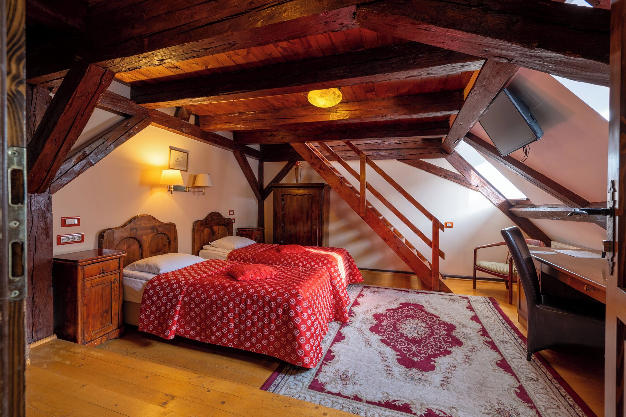 Un dormitorio con techo de madera, una cama con colcha roja, un escritorio y una silla.