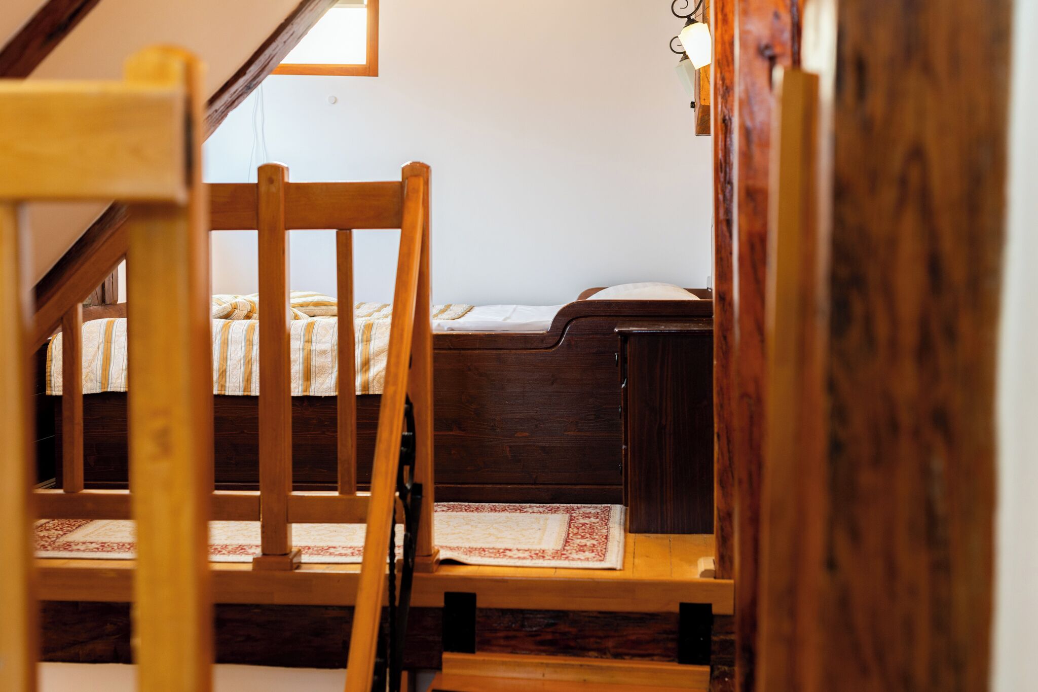 A bedroom with a wooden bed, a small bedside table, and a window with a view of the outside.