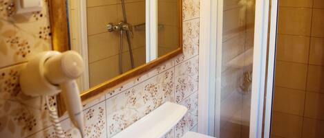 Un baño con un lavamanos blanco, un espejo con marco dorado y zona de ducha.
