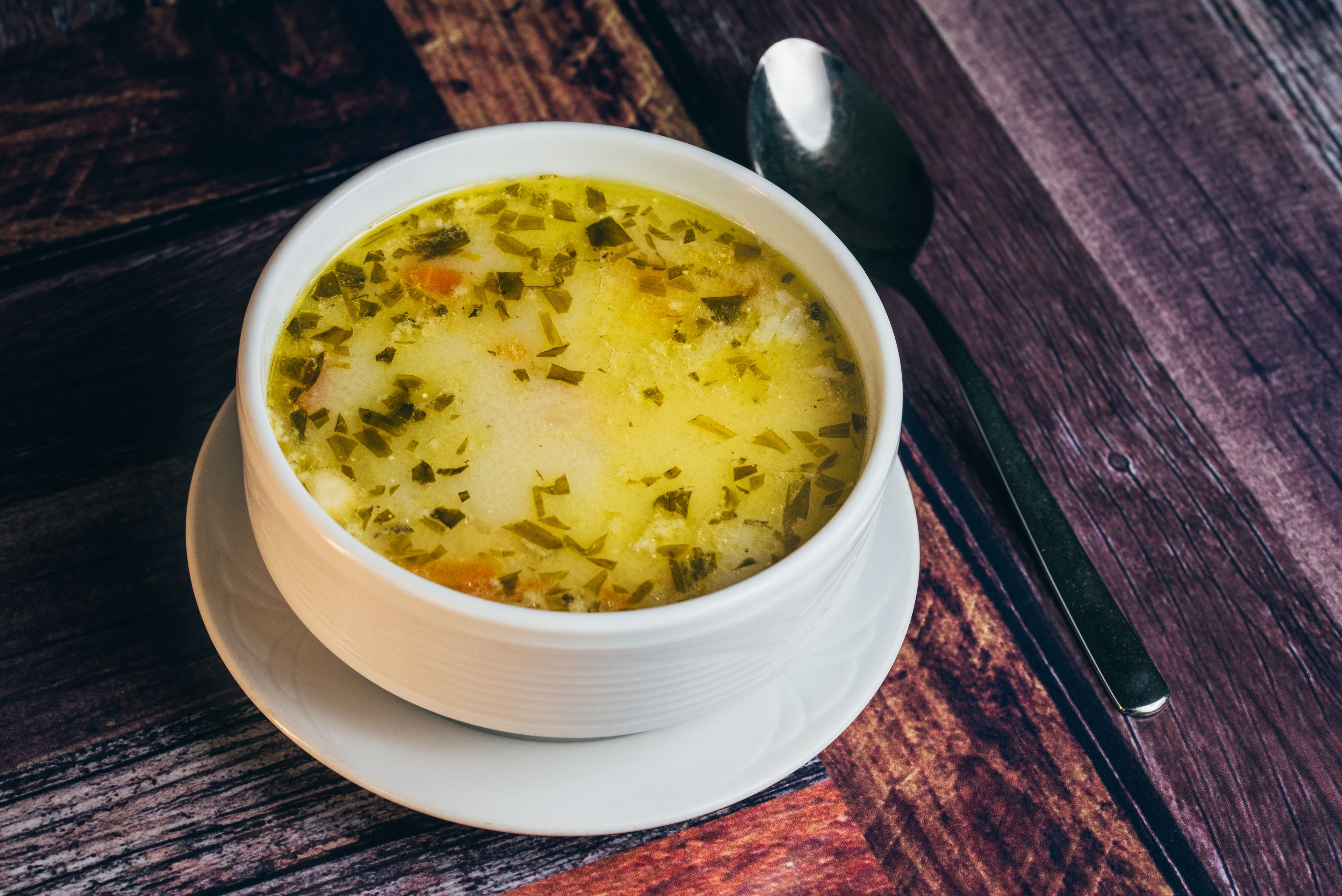 Un tazón de sopa sobre una mesa de madera con una cuchara.