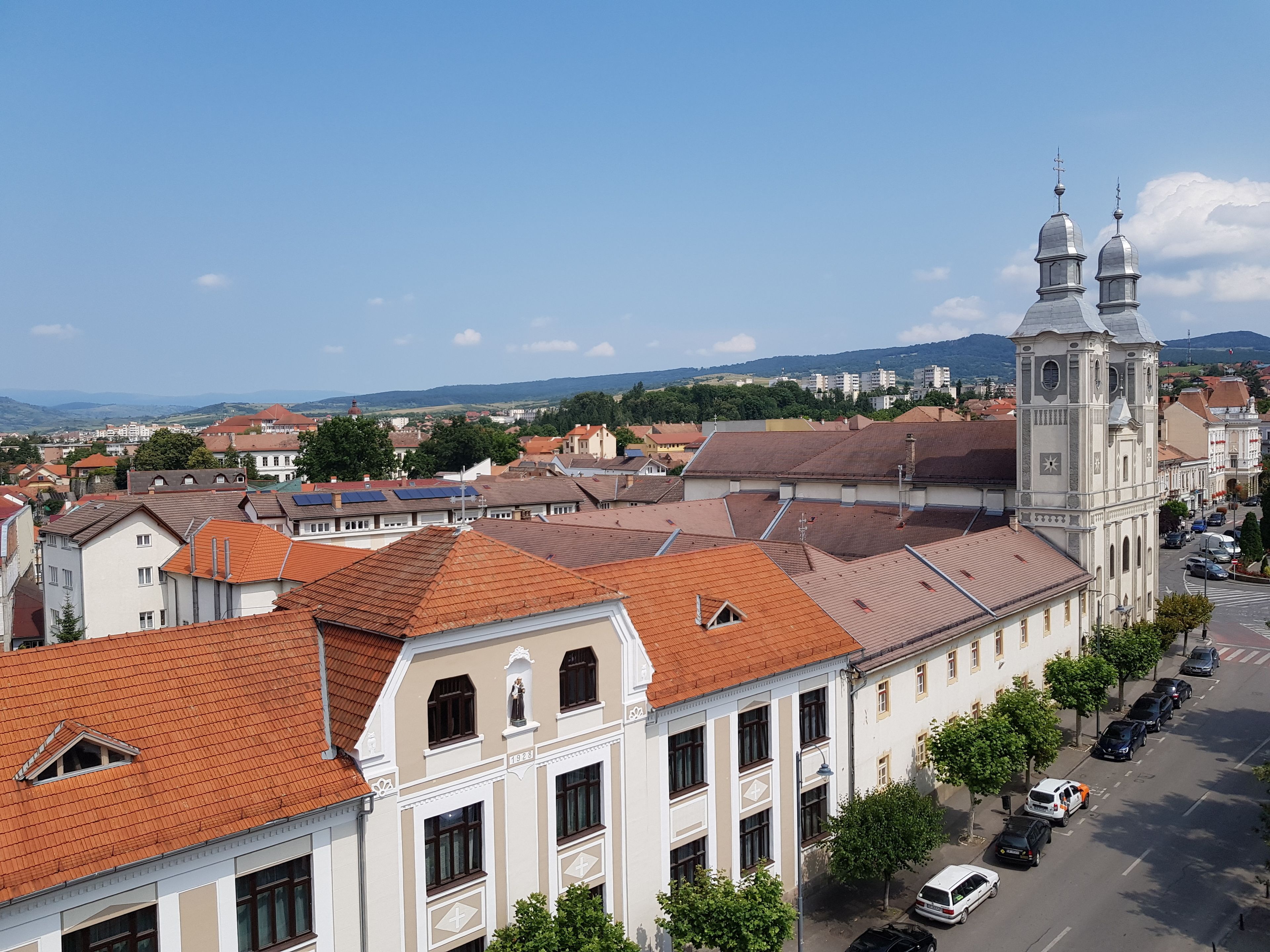 A historic building with a clock tower, surrounded by a street with parked cars and trees.