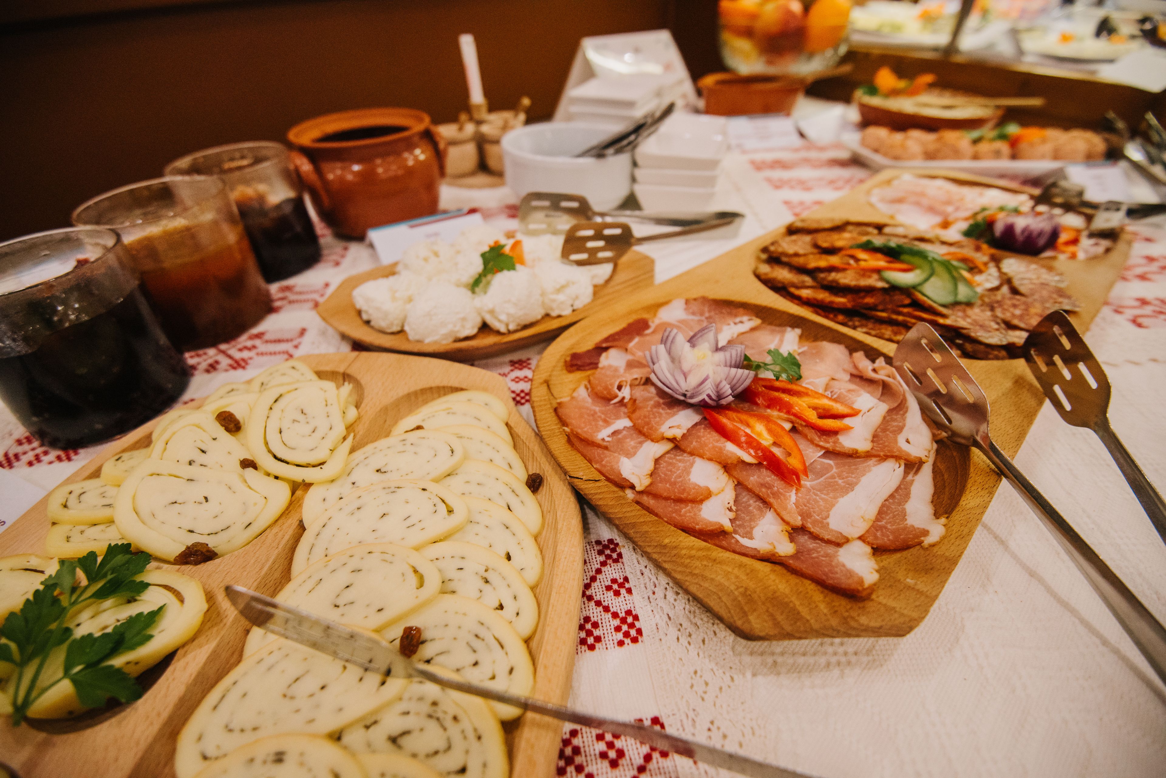 Un tavolo con diversi cibi e bevande, tra cui pane a fette, formaggio e salumi, insieme a diversi bicchieri di una bevanda scura.