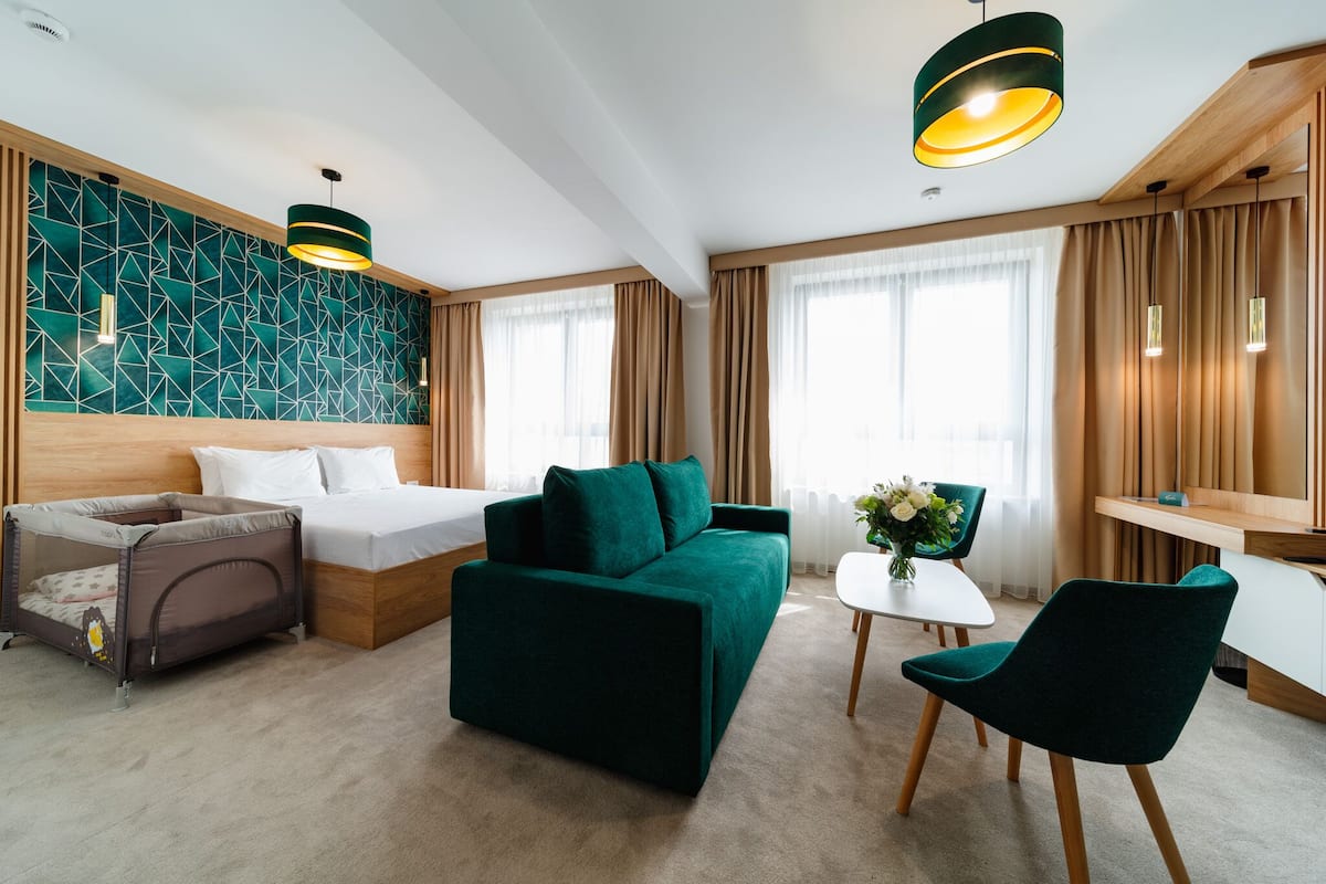 Ein modernes Hotelzimmer mit einem Bett, einem grünen Sofa, einem kleinen Tisch mit einer Vase und einem Sessel.