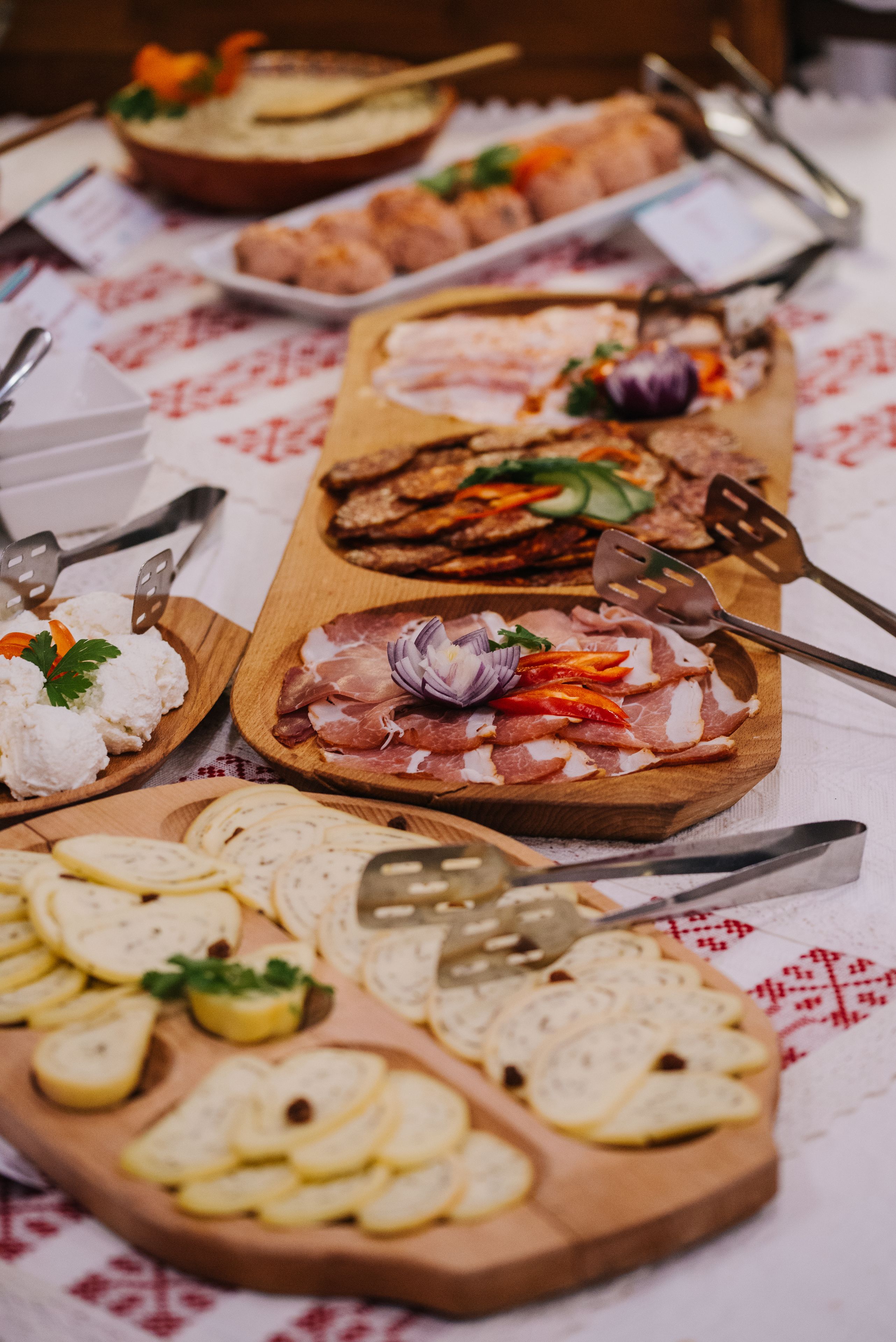 Variedad de alimentos en bandejas de madera, entre ellos carnes, quesos y frutas cortadas, dispuestos sobre una mesa con mantel estampado.