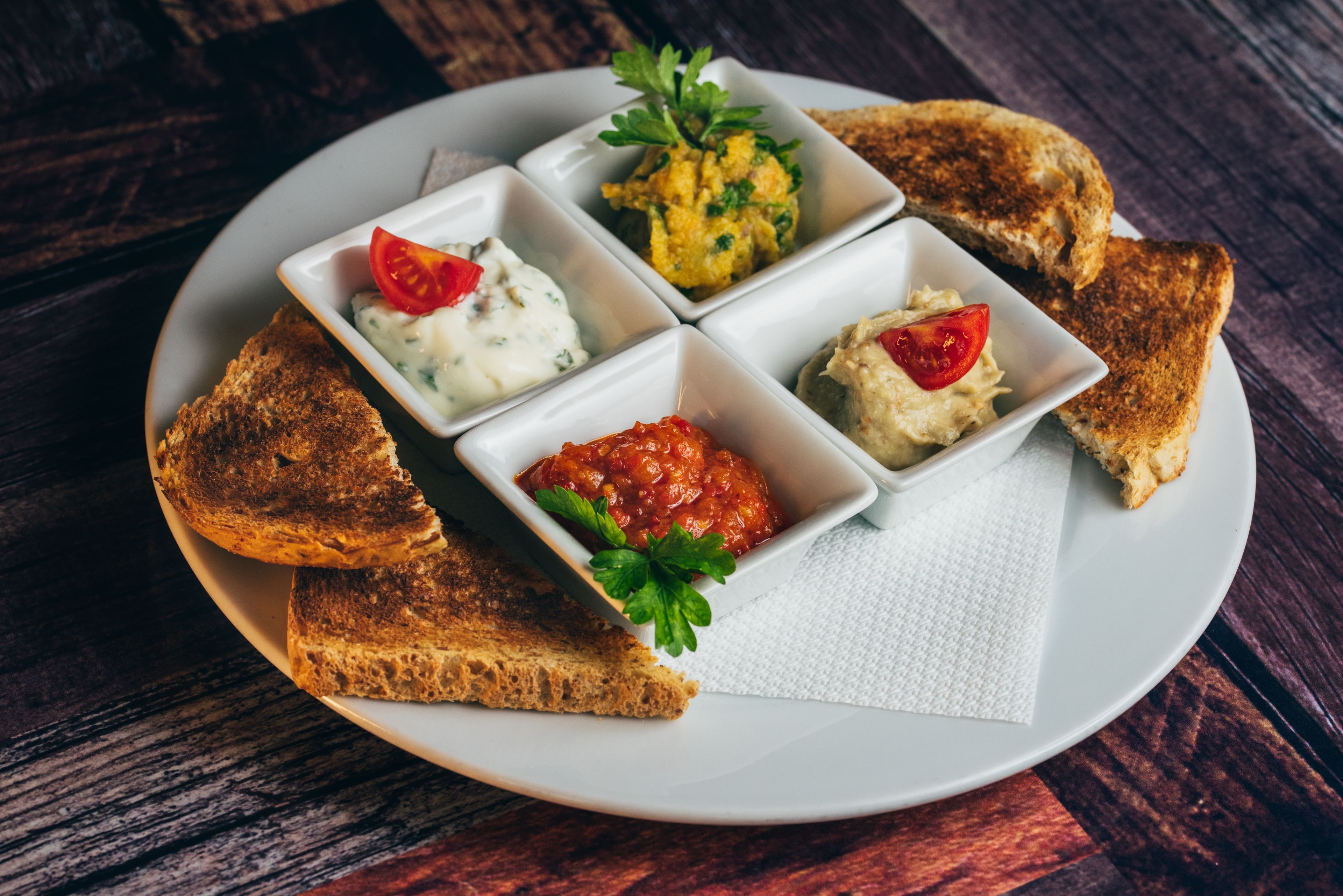A plate with four small bowls of different dips and toasted bread slices.