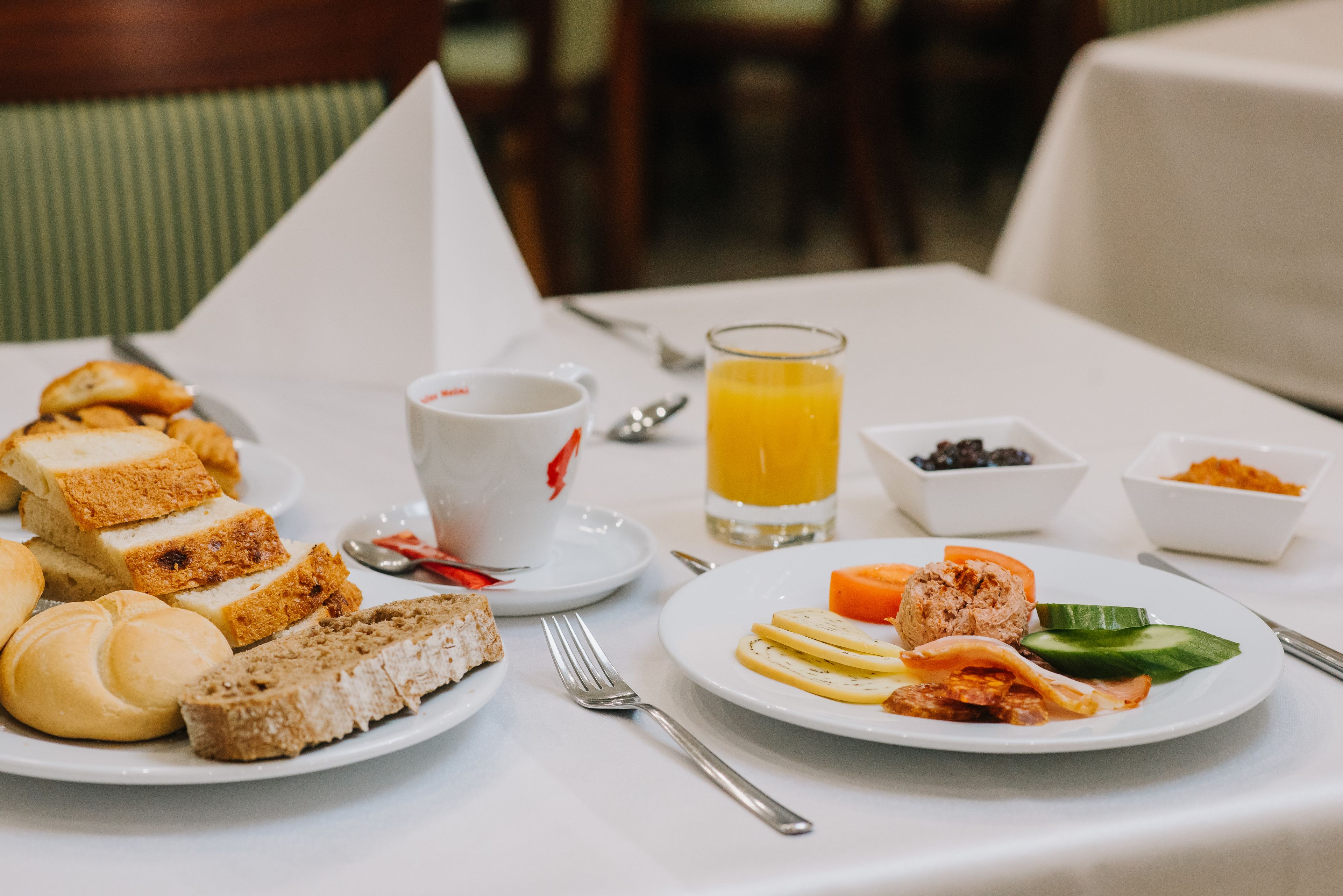 A breakfast setting with bread, pastries, a plate with eggs, vegetables, and a glass of orange juice.