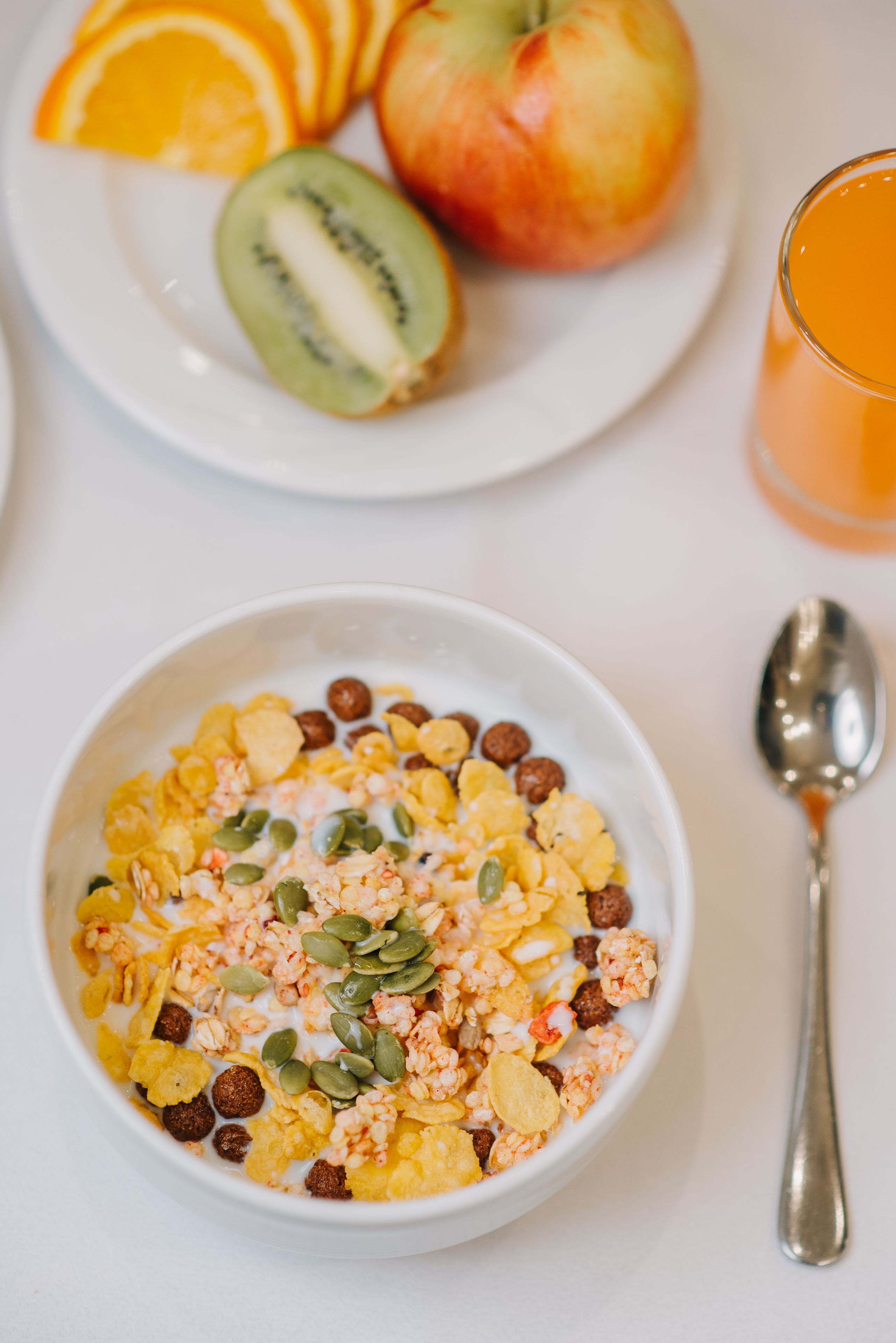 A bowl of cereal with milk and seeds, a plate with sliced fruit, and a glass of orange juice.