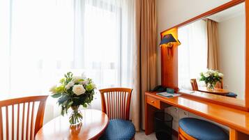 Habitación de hotel con escritorio de madera, dos sillas, un florero con flores, una lámpara y un espejo grande.