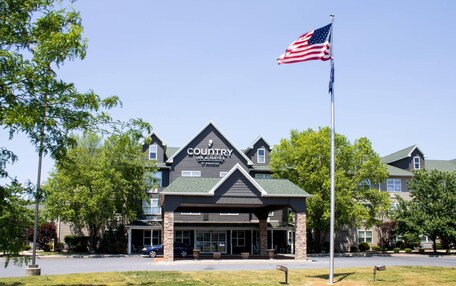 A Country Inn & Suites building with a prominent American flag, surrounded by trees and a parking lot.