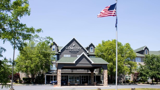 Ein Country Inn & Suites Gebäude mit einer großen amerikanischen Flagge, umgeben von Bäumen und einem Parkplatz.