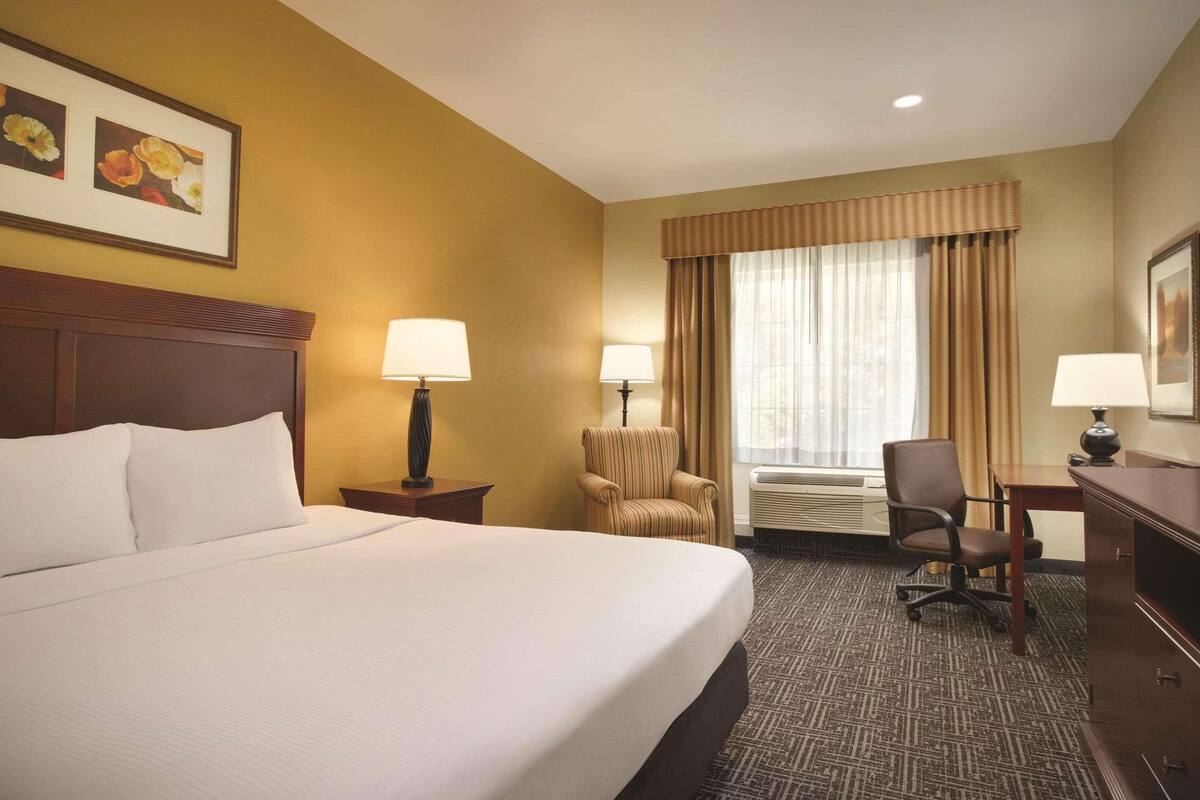 A hotel room with a large bed, two bedside lamps, a chair, a desk, and a window with curtains.