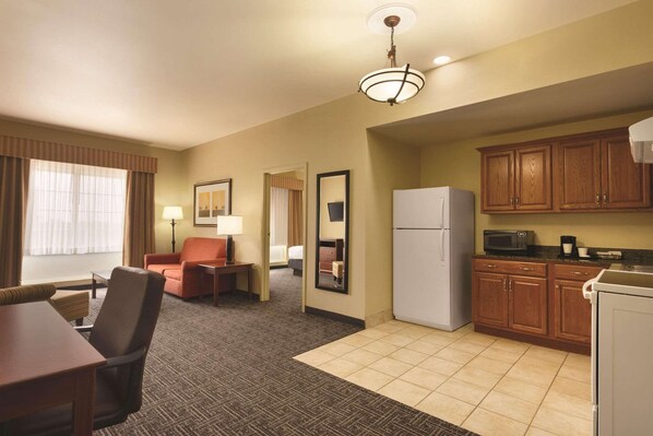 A hotel room with a dining area, kitchenette, and a large mirror.