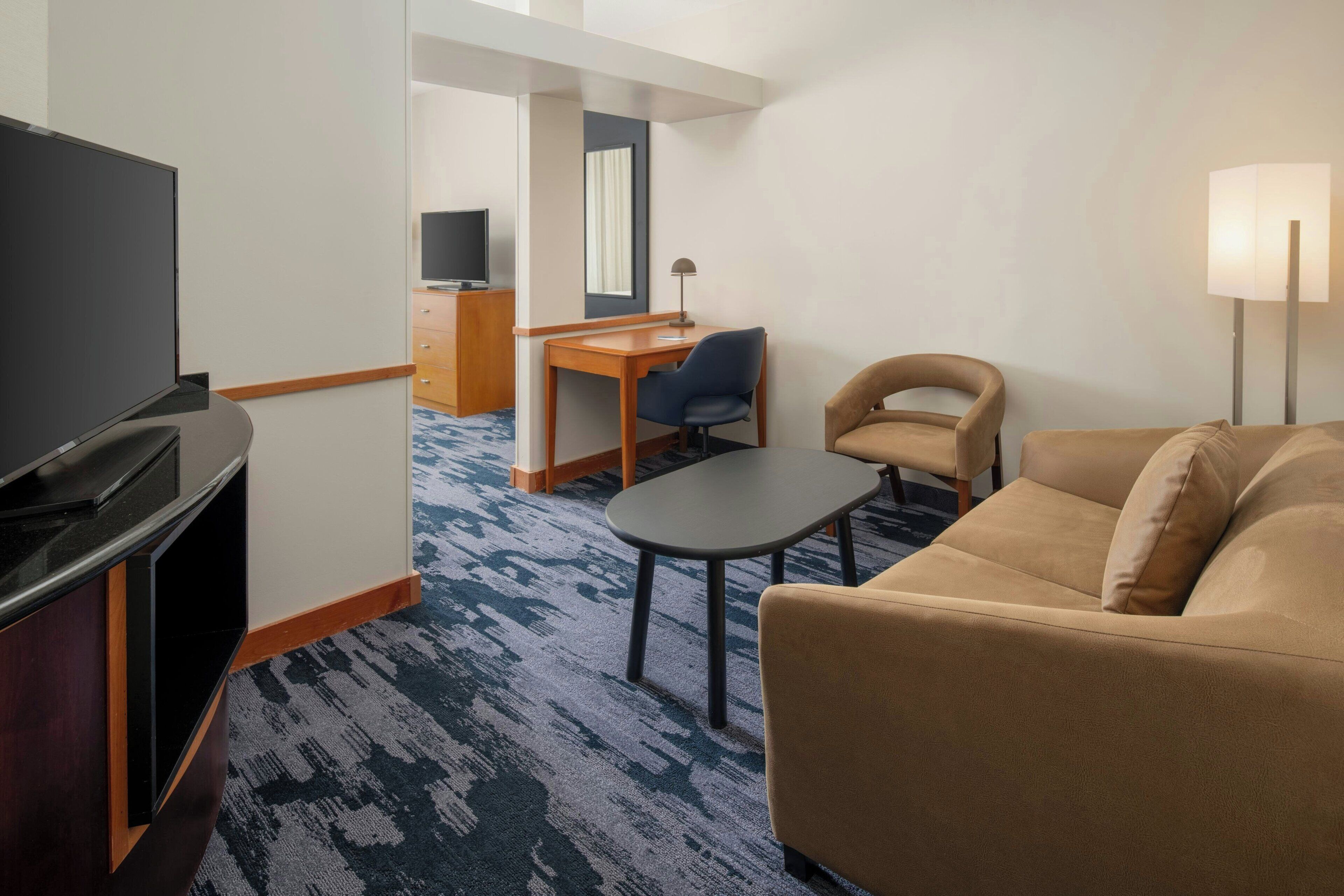 A hotel room with a TV, a desk with a chair, a sofa, and a lamp.