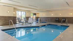 Une piscine rectangulaire intérieure à l’eau d’un bleu limpide, entourée de chaises longues et d’un espace baigné de lumière naturelle grâce à de grandes fenêtres.