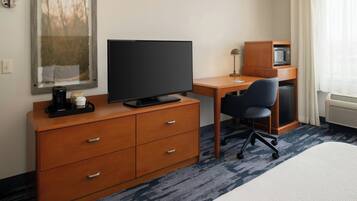 Quarto de hotel com escrivaninha, televisão, micro-ondas, cafeteira e uma cadeira.
