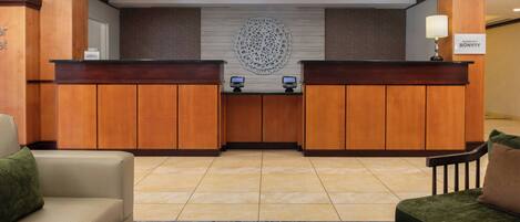 A reception area with wooden reception desks, a large decorative wall piece, and a seating area with a round table.