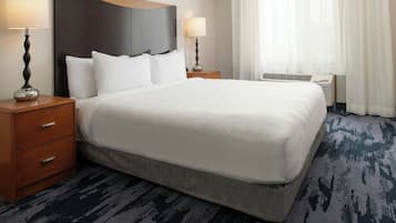 A hotel room with a large bed, two bedside tables with lamps, a wooden headboard, a window with curtains, and a carpeted floor.