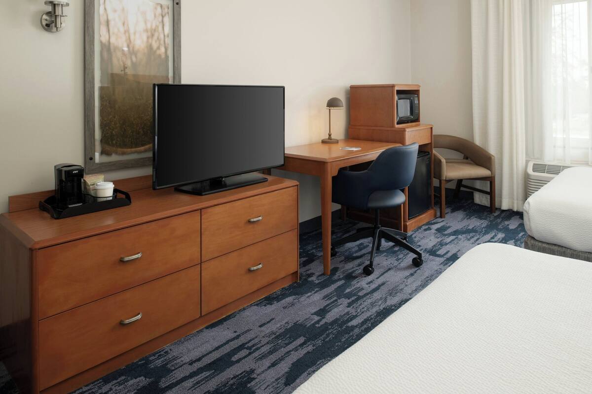 A hotel room with a bed, a desk with a computer, a chair, a television, a coffee maker, and a microwave.