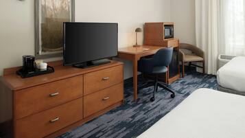 A hotel room with a bed, a desk with a computer, a chair, a television, a coffee maker, and a microwave.