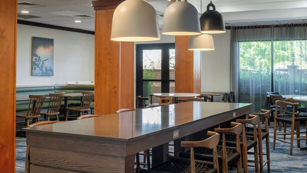 Un hall d’hôtel moderne avec un long comptoir de réception en bois, de nombreux tabourets de bar et des luminaires suspendus.
