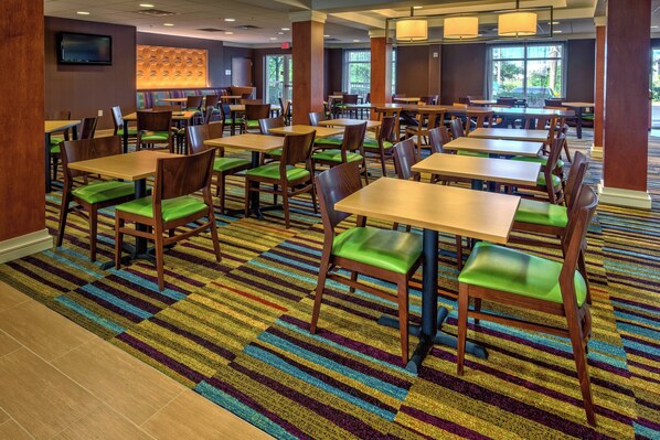 A spacious dining area with multiple tables and chairs, a patterned carpet, and large windows allowing natural light.