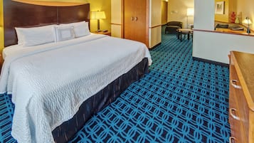 A hotel room with a large bed, a wooden headboard, a desk with a chair, and a patterned carpet.