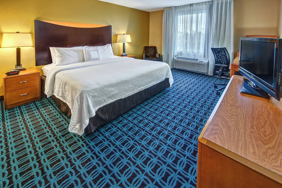 Quarto de hotel com uma cama grande, luminárias de cabeceira, uma escrivaninha com televisão e uma janela com cortinas.
