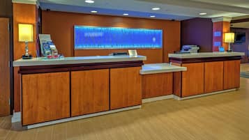Zona de recepción de un hotel con un mostrador de madera, una gran estructura mural iluminada y un televisor de pantalla plana.