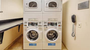 A laundry facility with two stacked washing machines and a phone for emergencies.